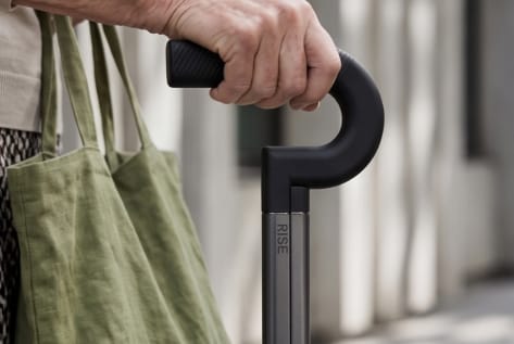 A hand resting on the Rise cane handle beside a tote bag
